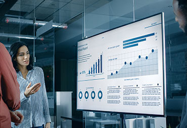 IT Leaders ﻿Analyzing Statistics, Charts and Pies with Company's Growth Shown on a Wall TV