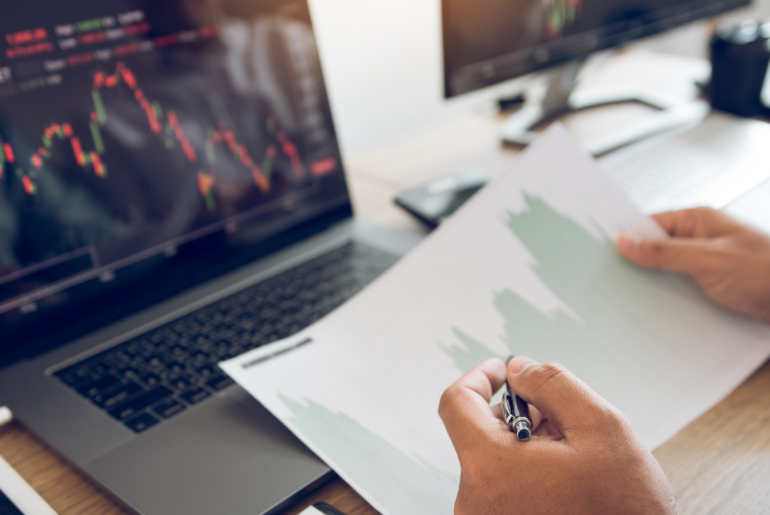 Person's hands shown looking at a graph on printed paper, resting on a laptop keyboard