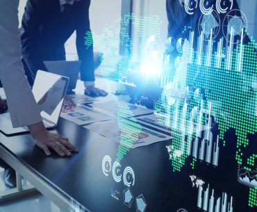 people hovering over a table, you can't see their faces, in a boardroom, with graphs and the globe overlaid on top