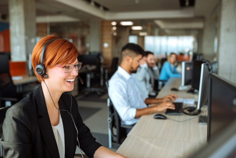 people working on computers in an open-concept office, leading woman on a headset