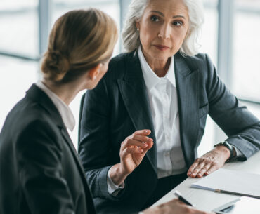 Two female executives in business suits having a serious conversation at a conference table, symbolizing CEO and CMO misalignment on growth priorities