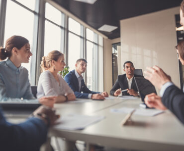 Executive leading a business meeting with colleagues around a conference table in a modern office.