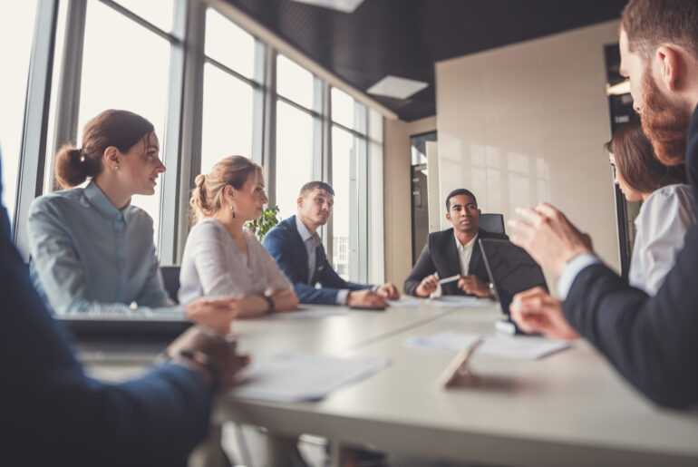 Executive leading a business meeting with colleagues around a conference table in a modern office.