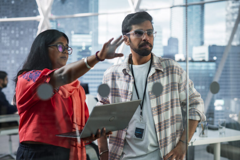 Two business professionals collaborating on strategy using a laptop in a modern office setting.