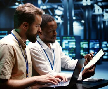IT professionals collaborating on AI-driven operations using laptops and tablets in a modern data center.